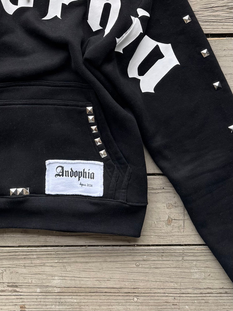 Close-up of Diamant Noir Studded Hoodieggg showcasing studs and logo detail on a black fabric.